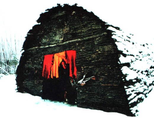 Ирокез в устрашающей маске на пороге традиционного священного длинного дома